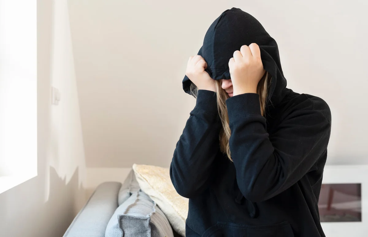 young woman covers her face with a hoody