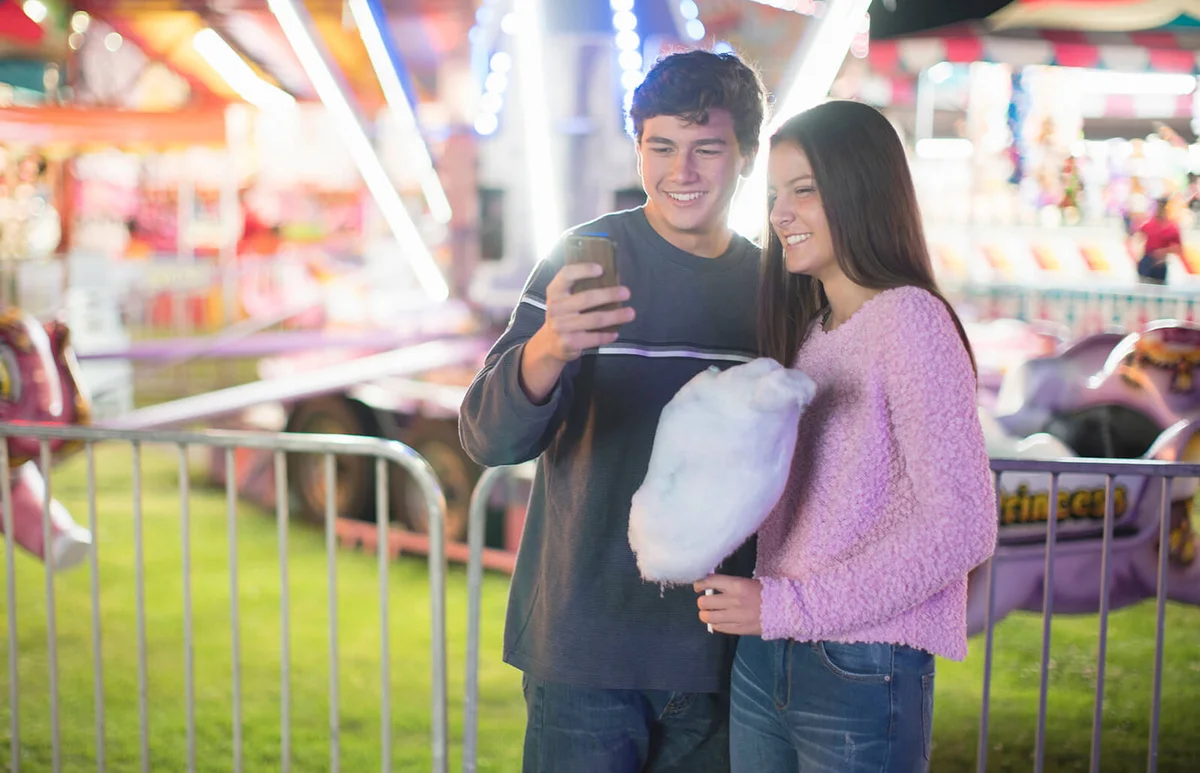teenage couple texting at a fair at night