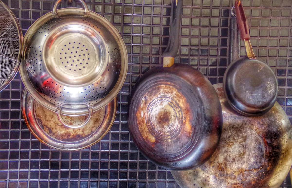 Saucepans And Kitchen Utensils Hanging On Backsplash At Home