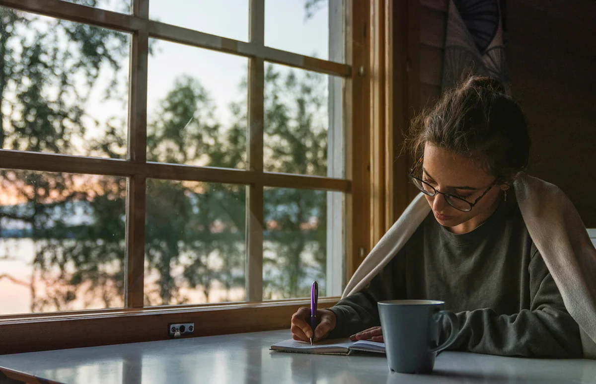 Woman sitting at the window at a lake writing into diary