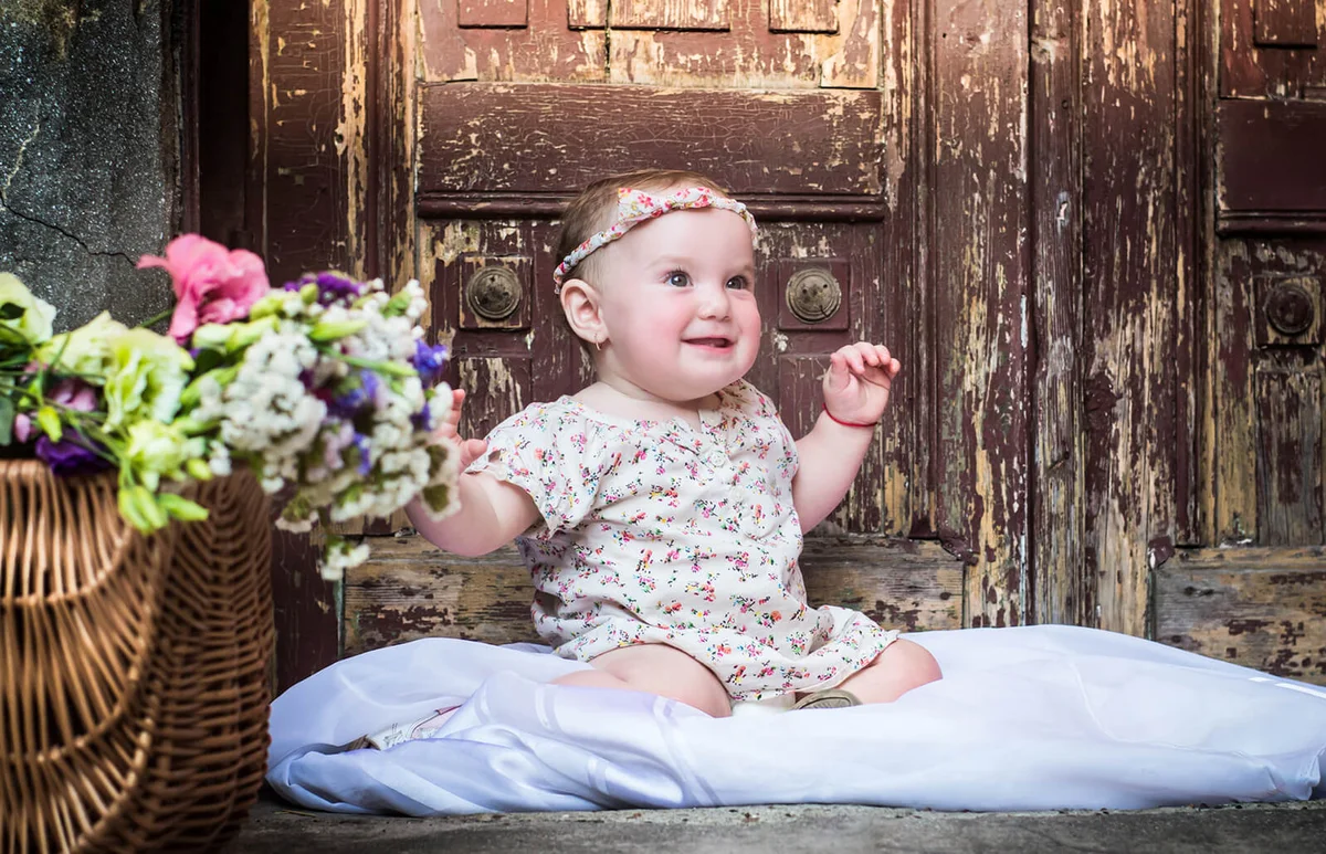 Cute Girl Sitting By Flowers Against Closed Door