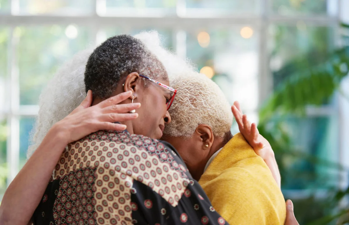 senior women hugging each other in leafy house