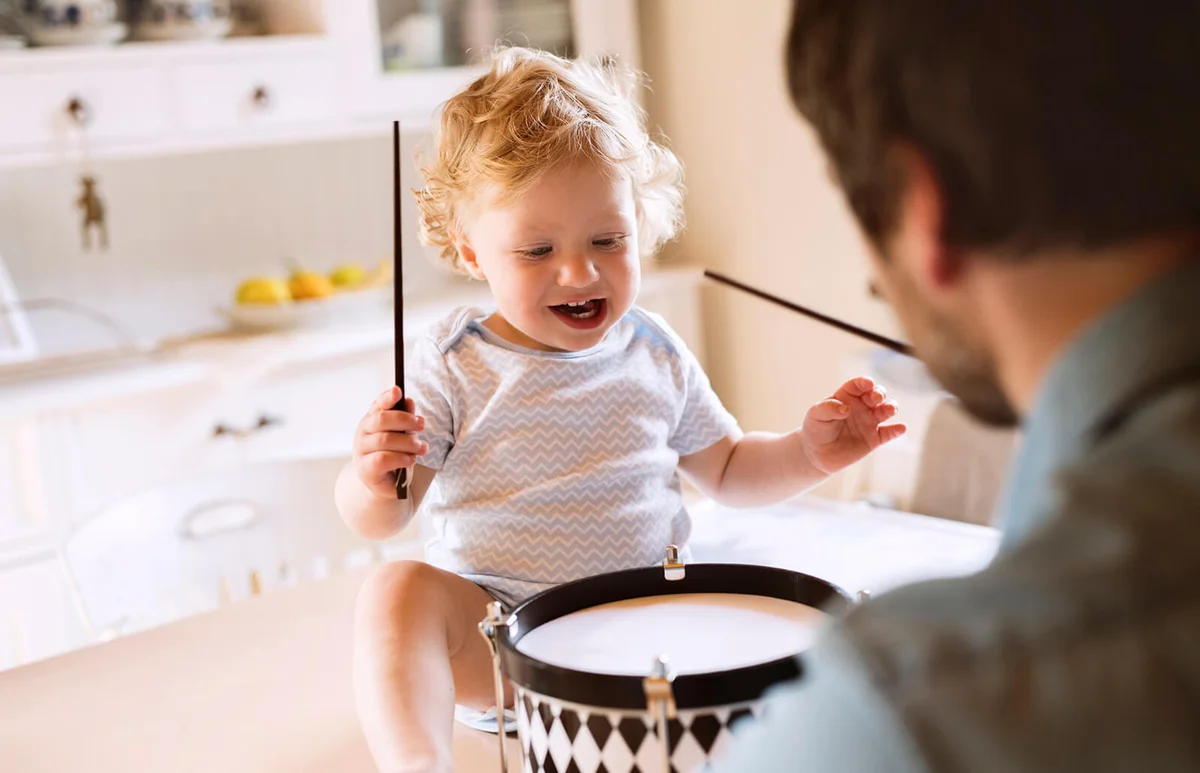Father with happy little boy sitting on kitchen table playing drum