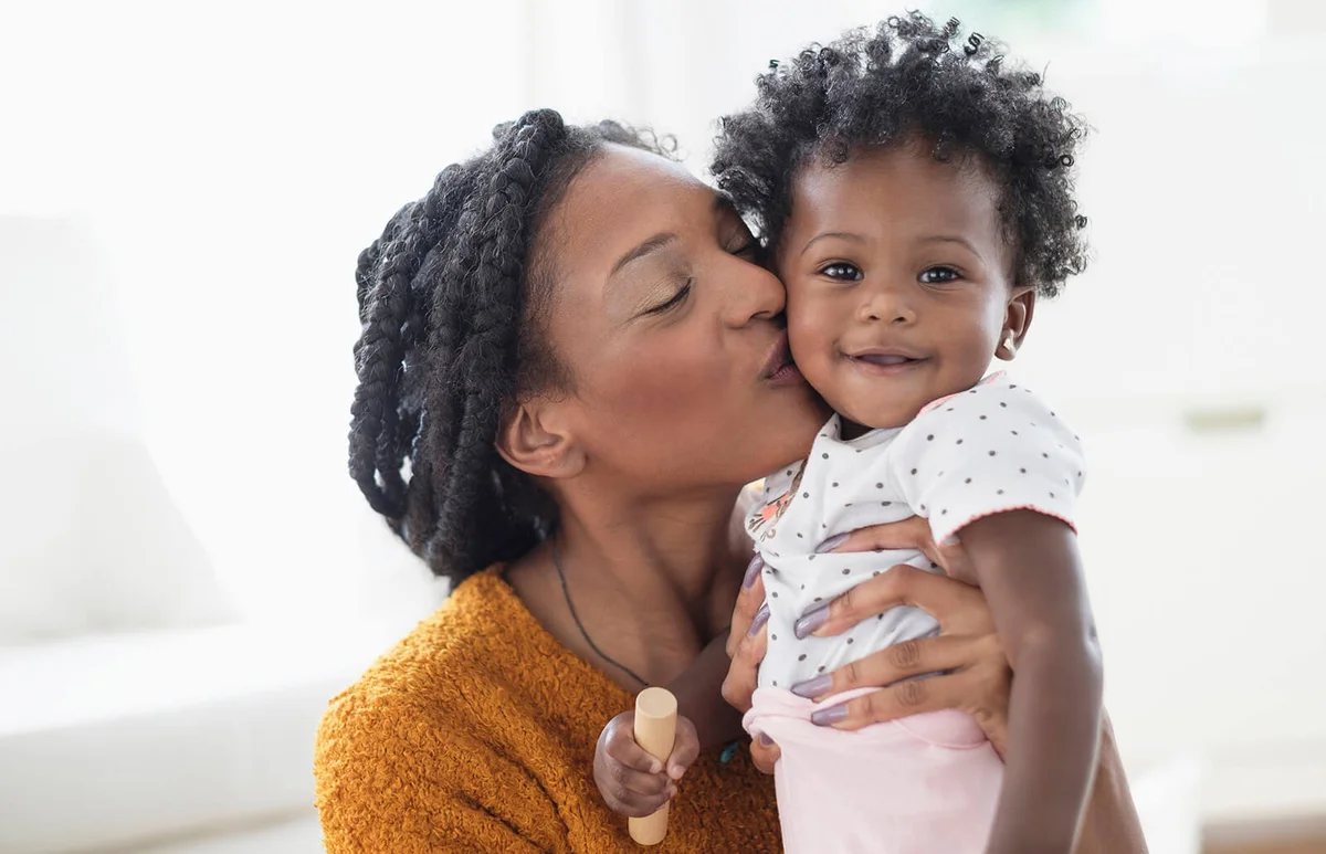Smiling mother kissing baby daughter on cheek