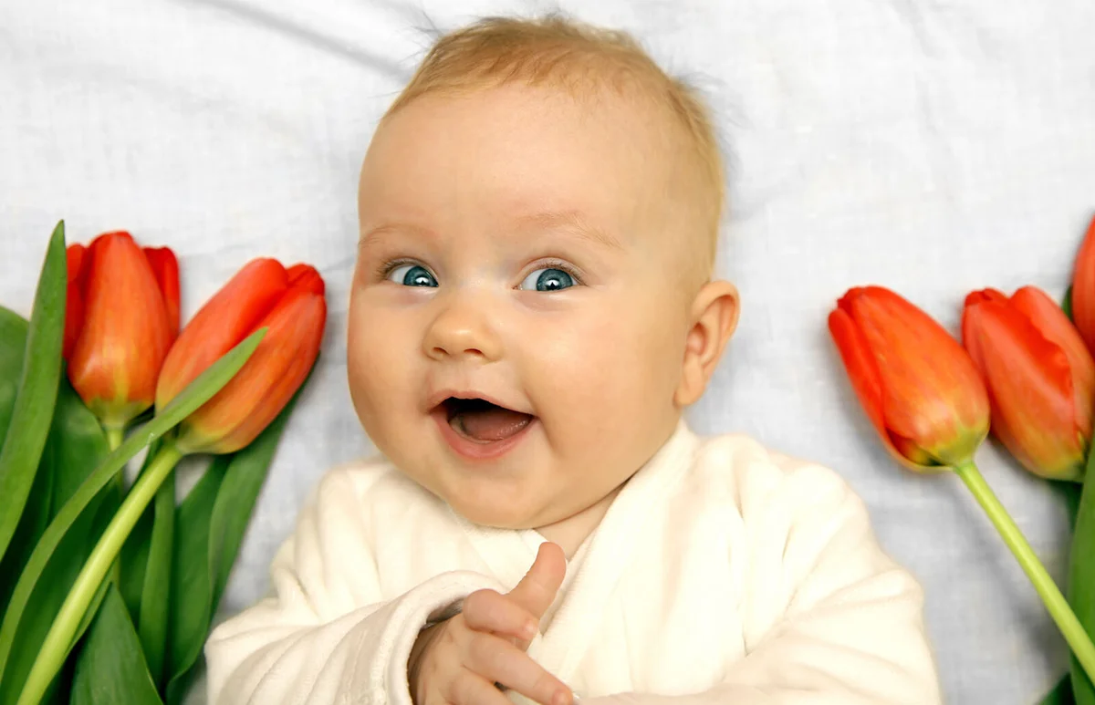 newborn baby laughing among red tulips