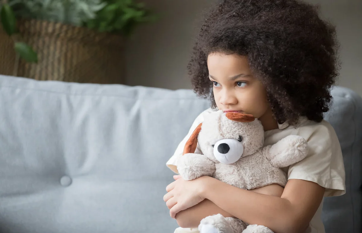 Upset lonely kid girl holding teddy bear looking away