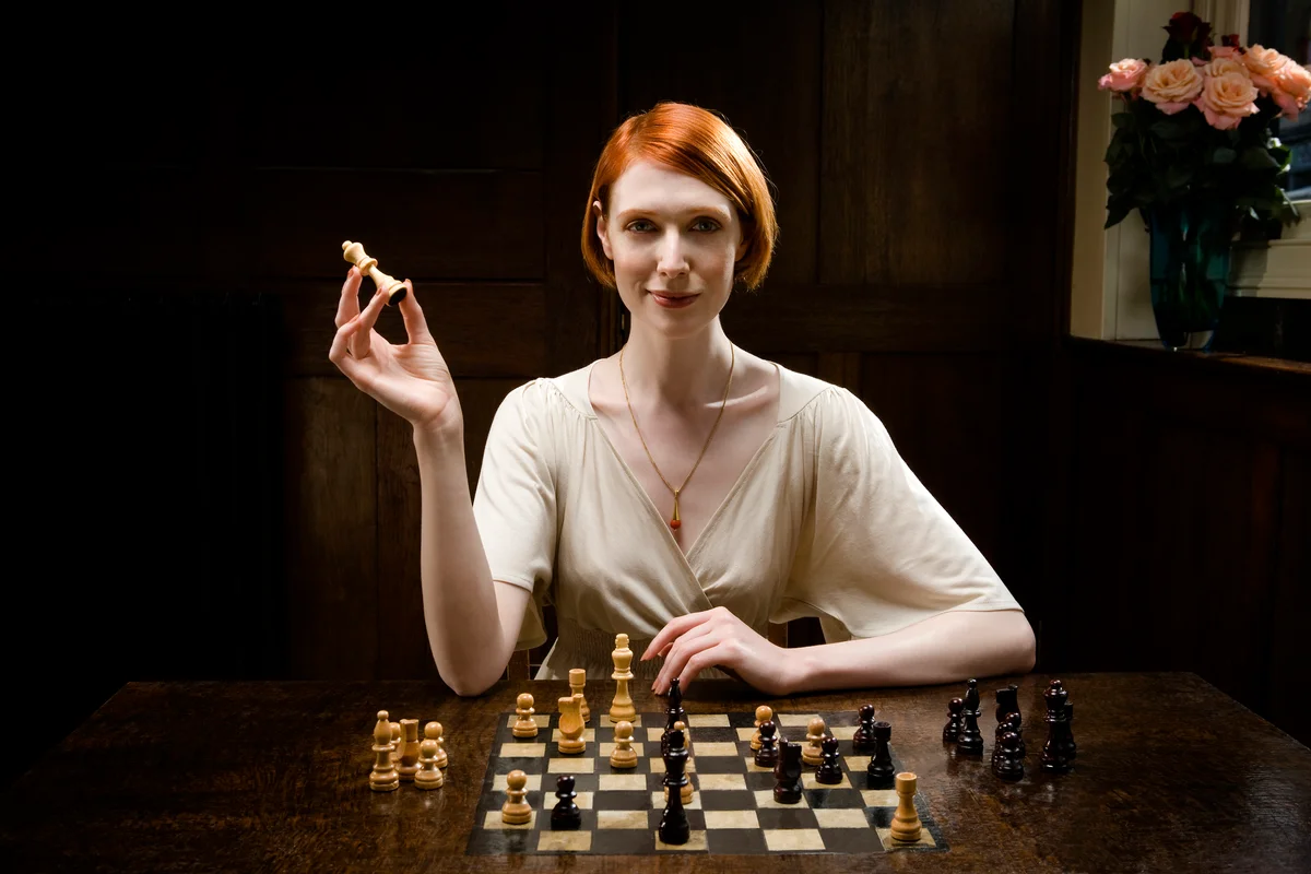 Woman holding up queen chess piece and smiling