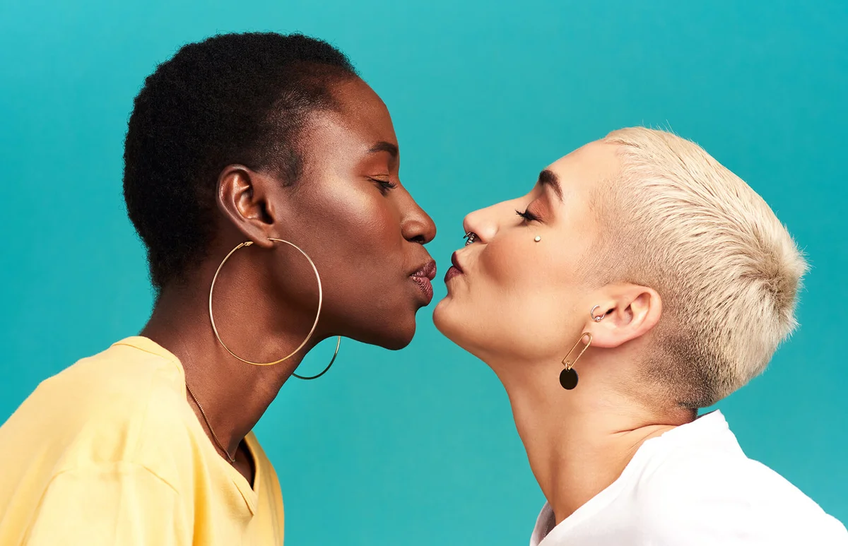 two young women kissing against a turquoise background