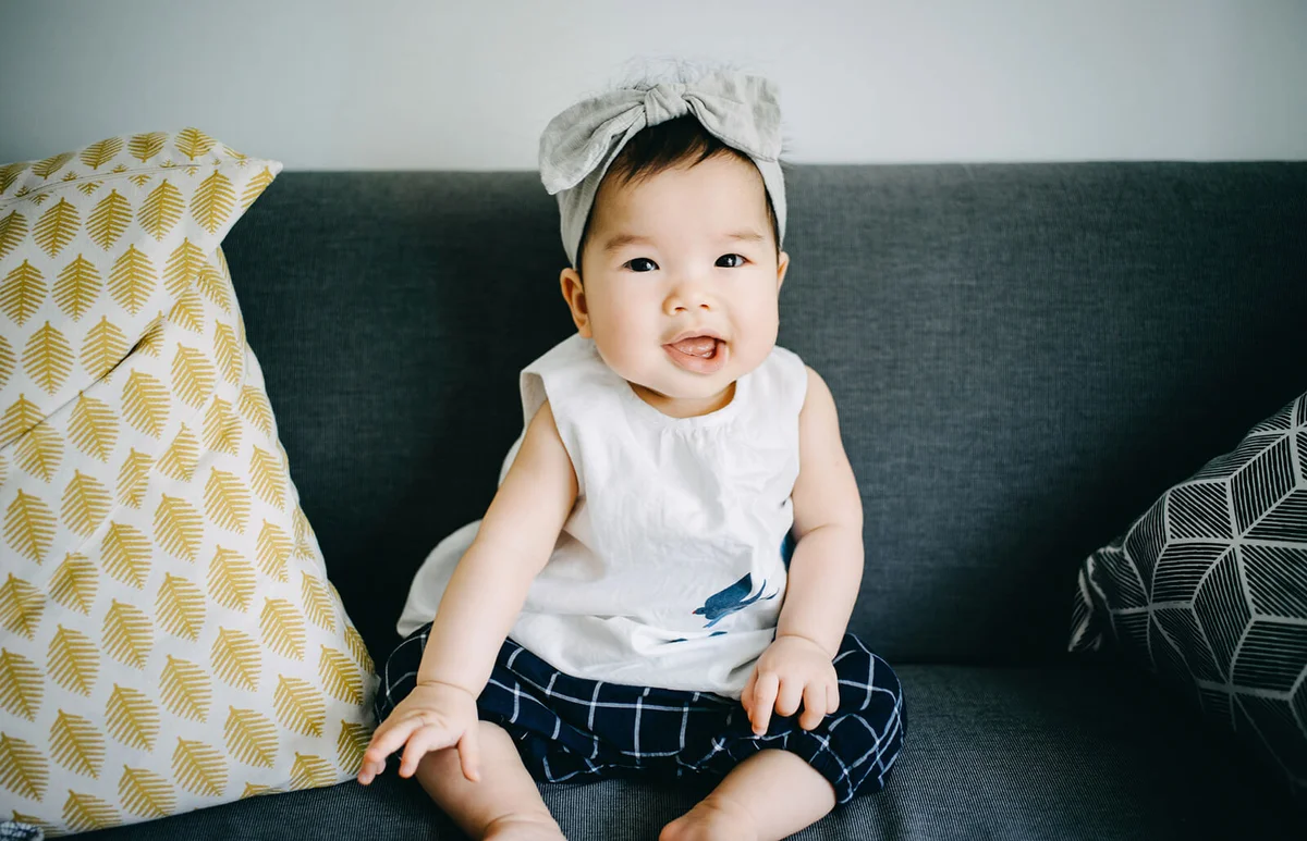 Adorable baby girl sitting on sofa and smiling joyfully