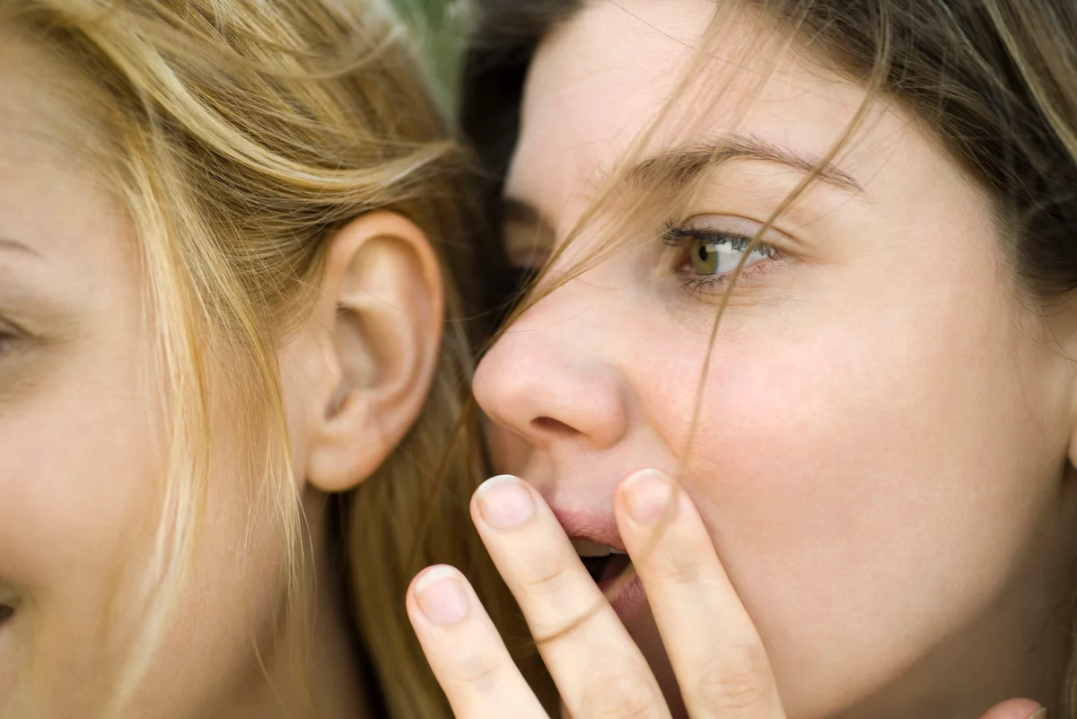 Young woman whispering secret into friend's ear
