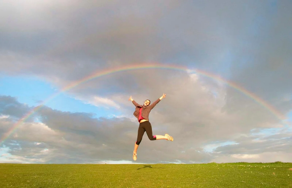 Young female hiker jumping mid air below rainbow