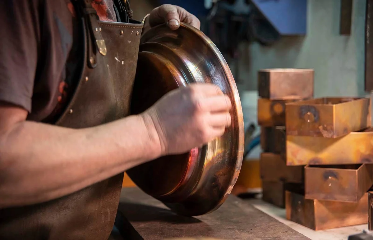 hands of the man wearing the leather apron who polishing the copper detail in the workshop