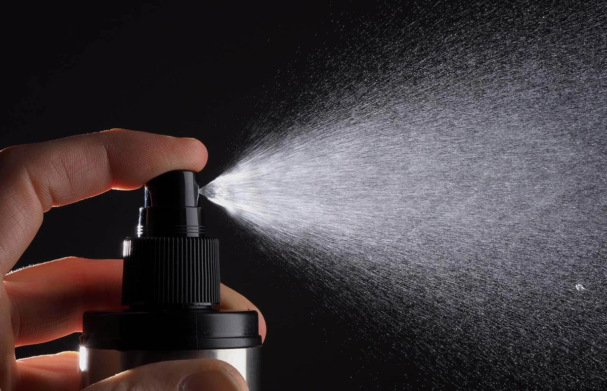 Cropped Hand Spraying Perfume Against Black Background