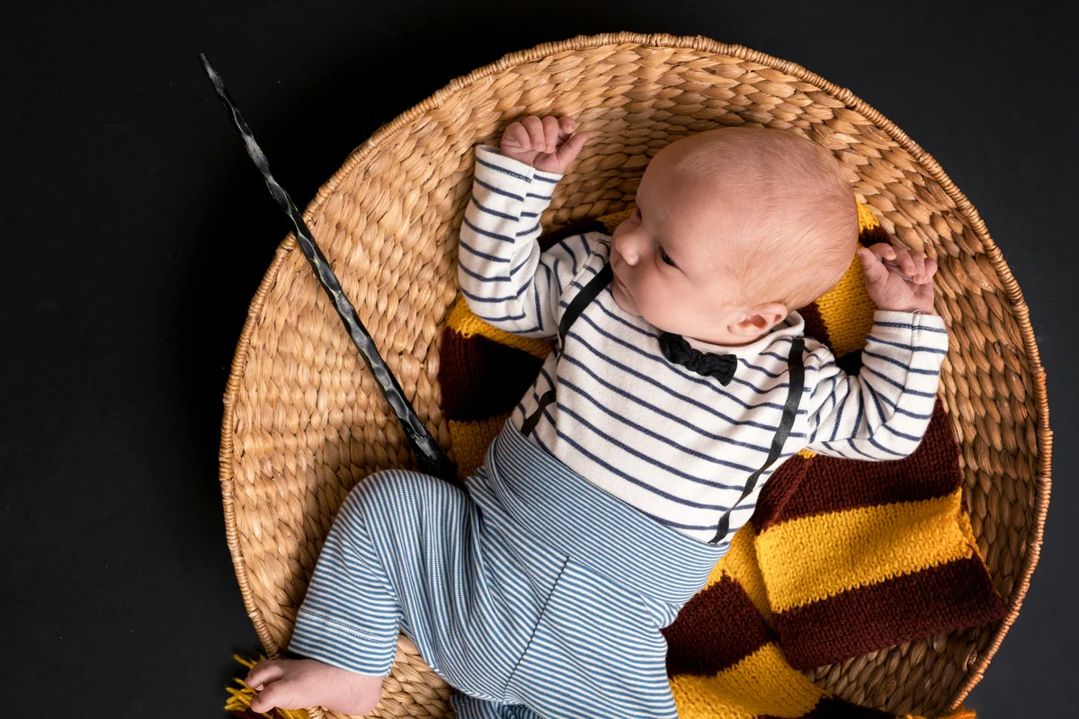 Little newborn baby boy with a magic wand, black background and scarf