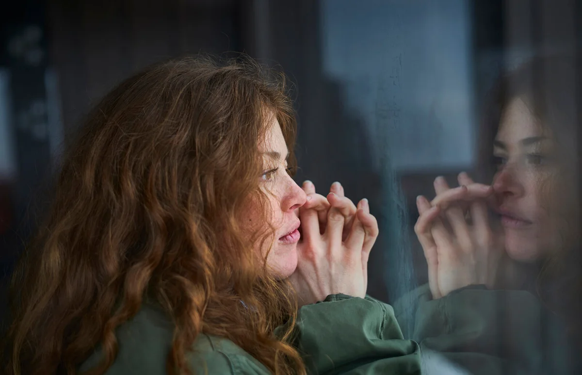 woman looking out of window into her reflection