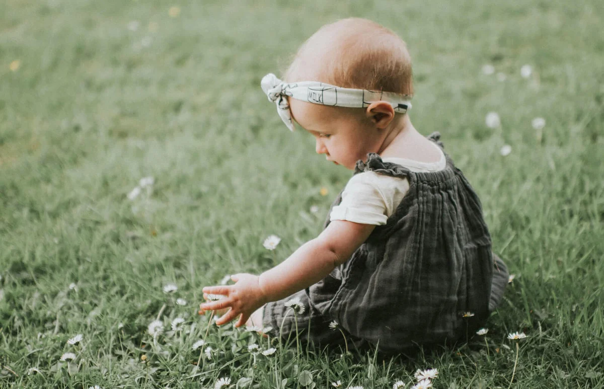 Baby girl sitting on grass with Daisies
