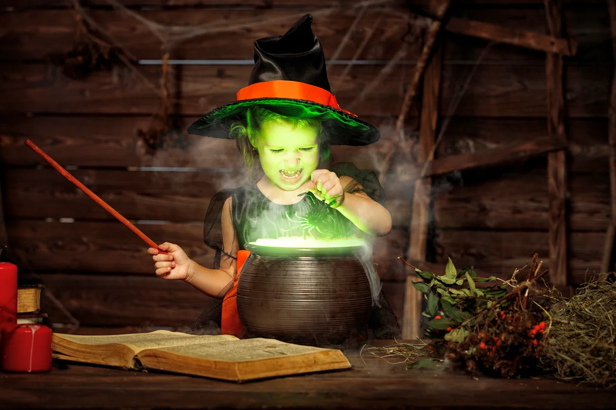 Little witch child cooking potion in cauldron with spell book