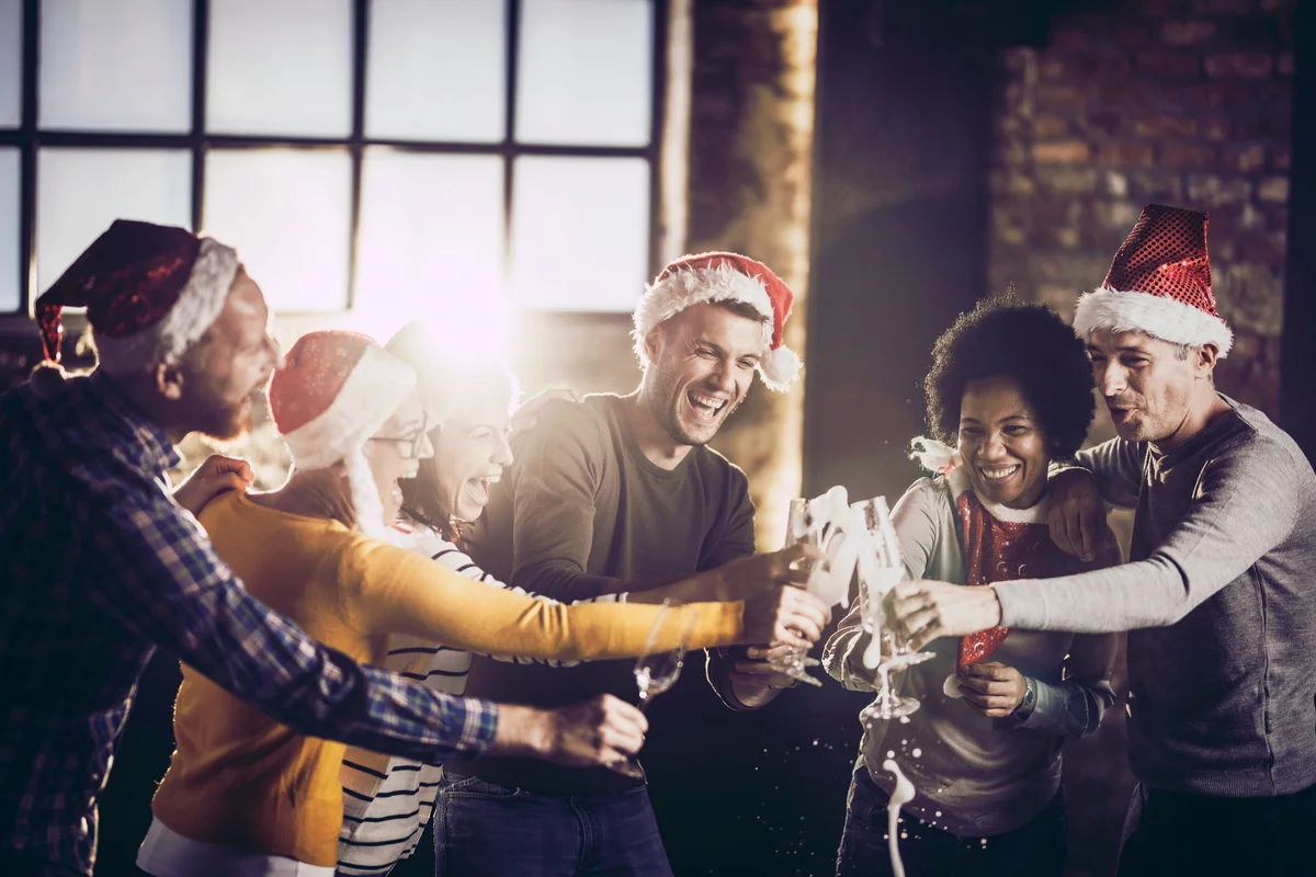 Joyful team having fun while opening champagne during Christmas celebration