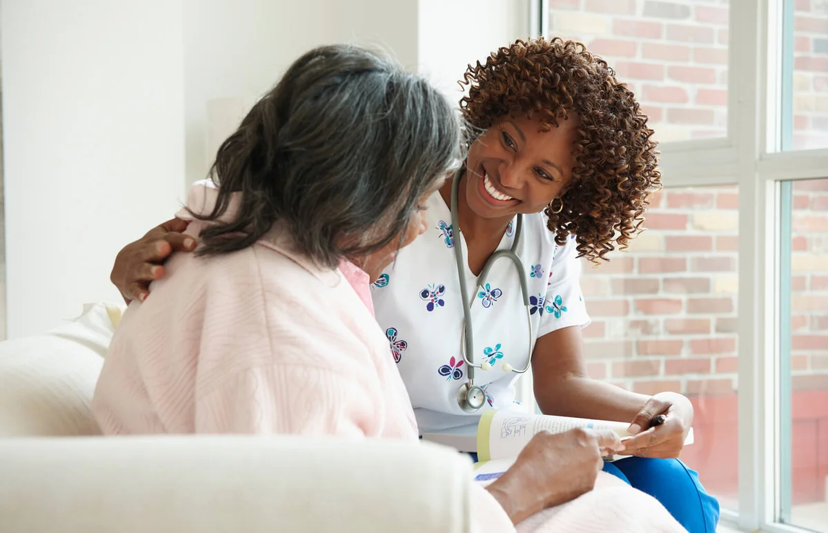 Smiling Nurse Looking At Book With Senior Patient