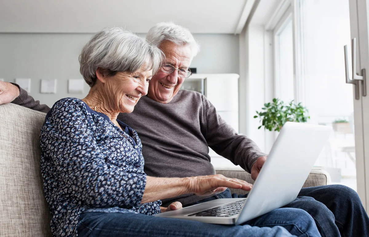 Happy senior couple sitting on the couch in the living room using laptop