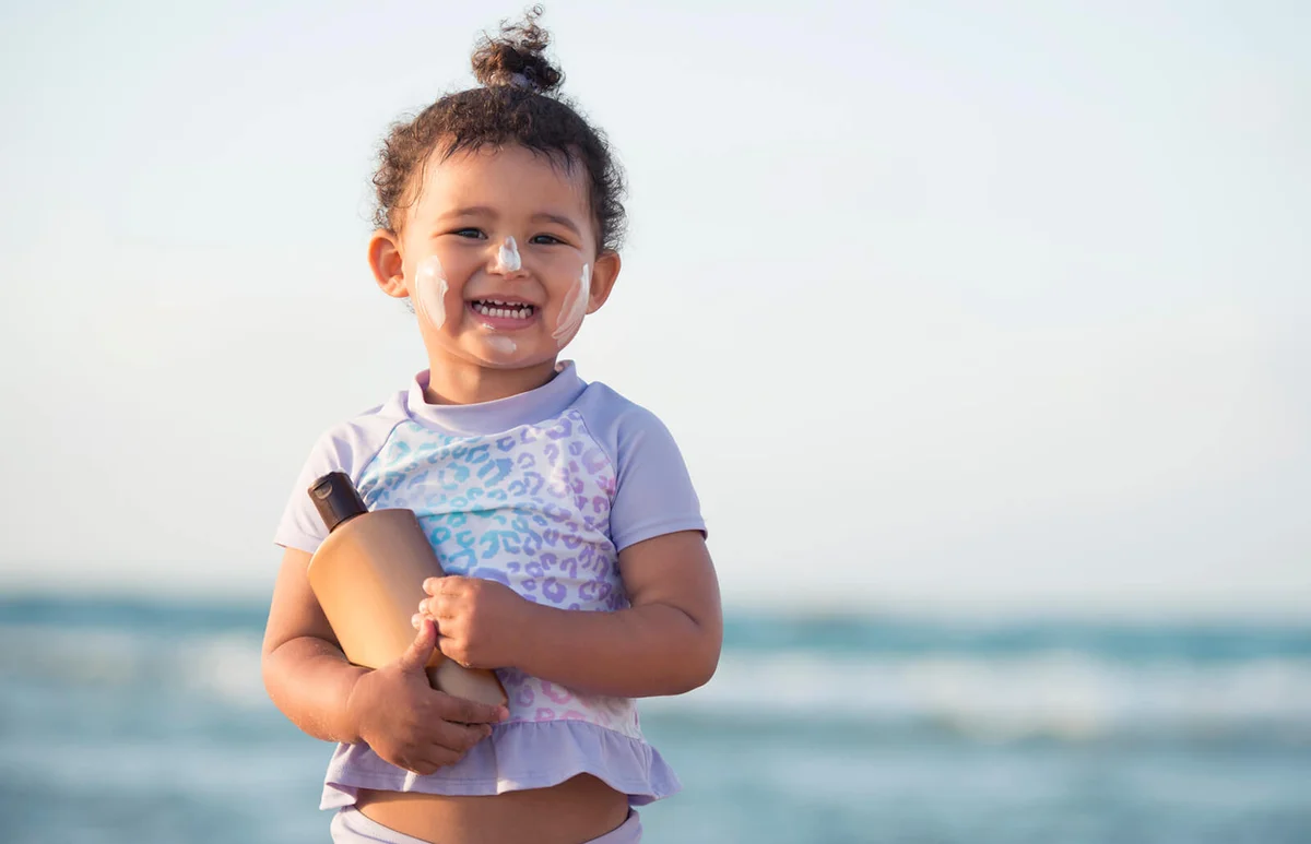 Kid with suncream bottle on sea beach
