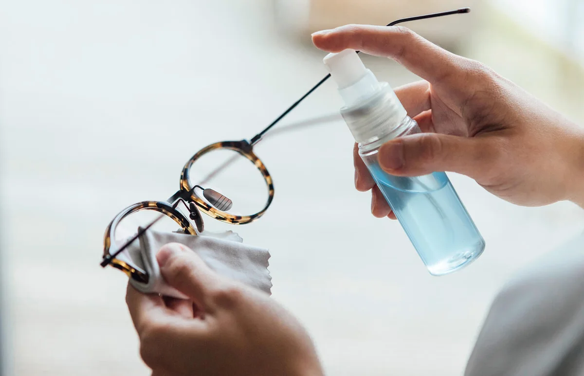 woman cleaning eyewear surface with sanitising spray