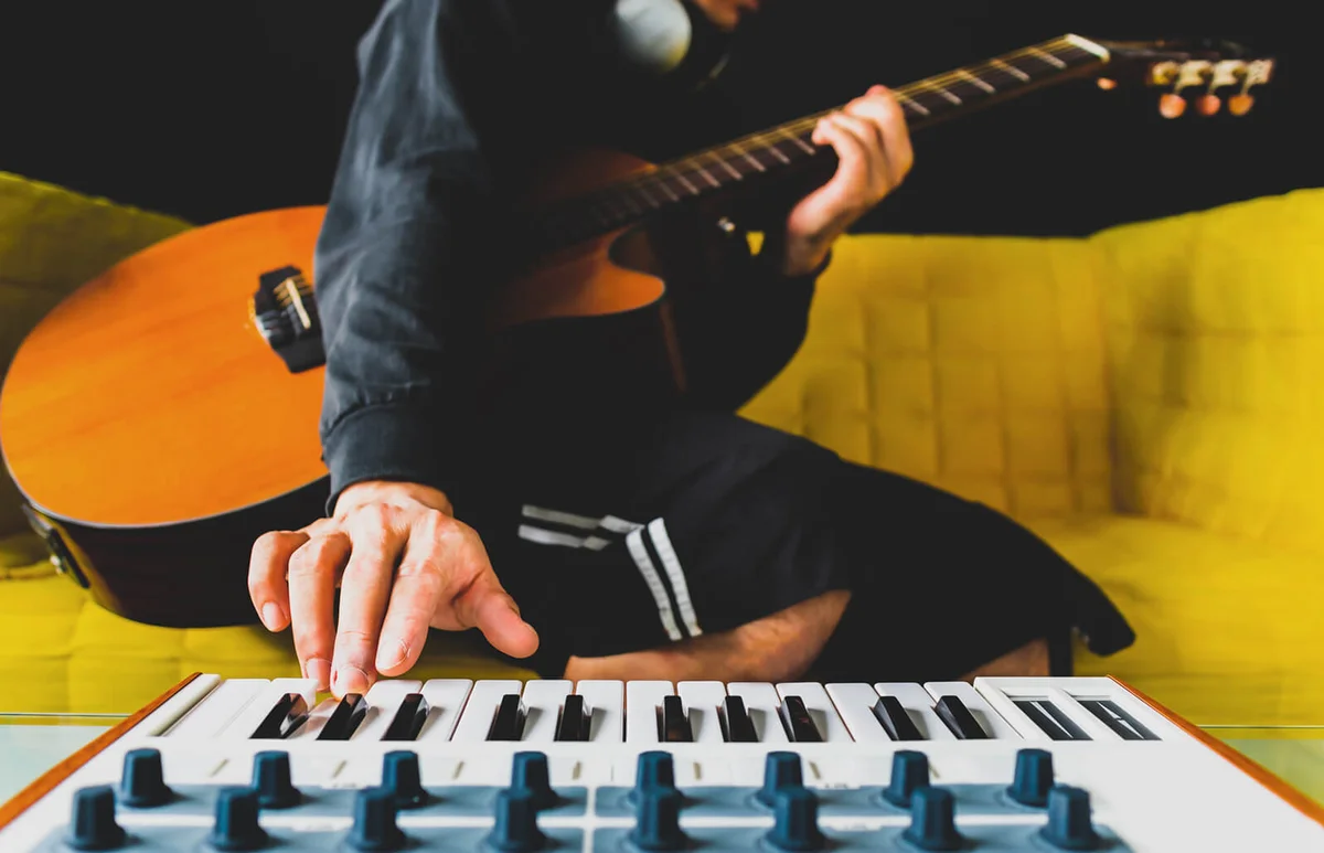 male songwriter playing guitar and keyboard for creating melody