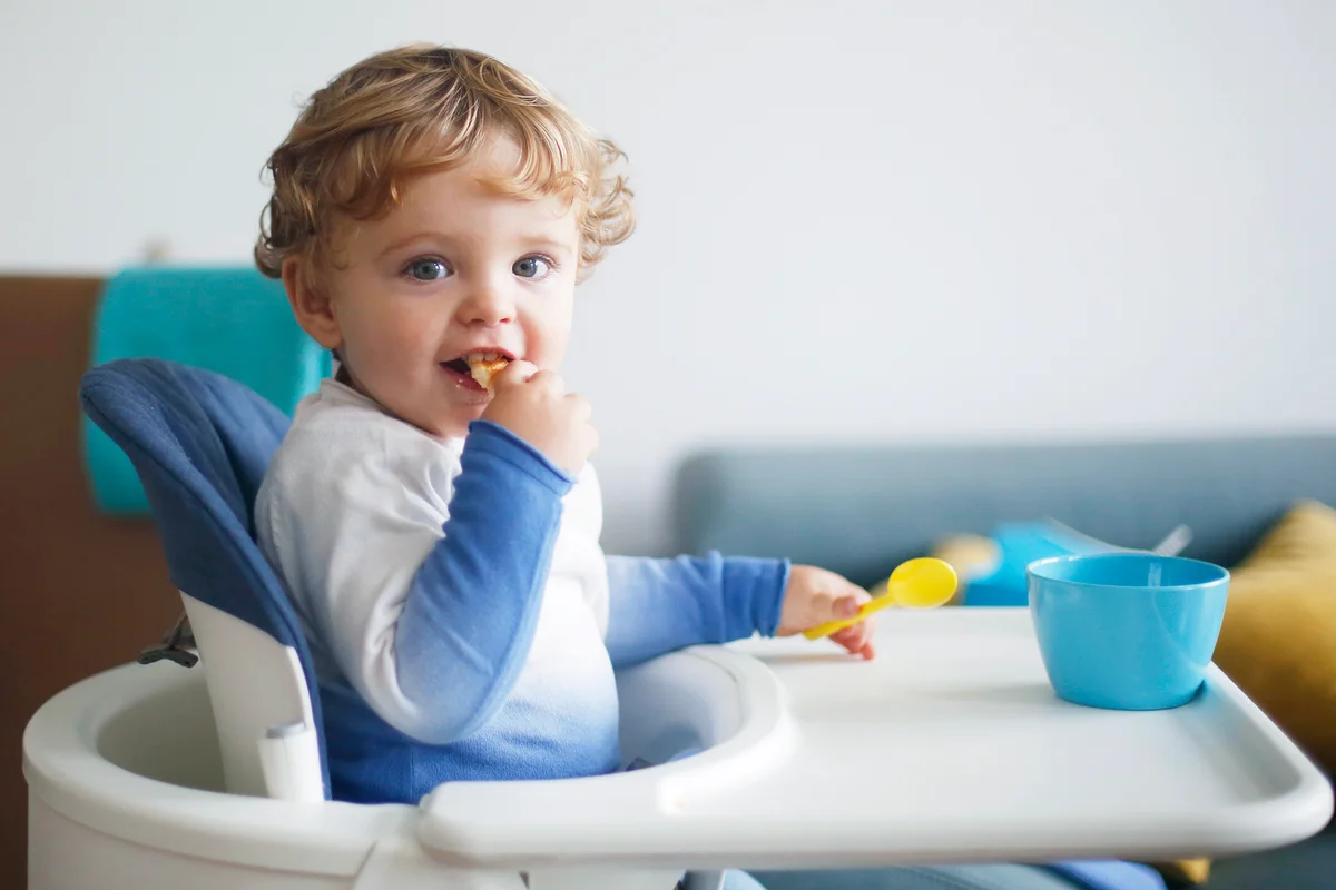 A 15 months old boy eating in his high chair