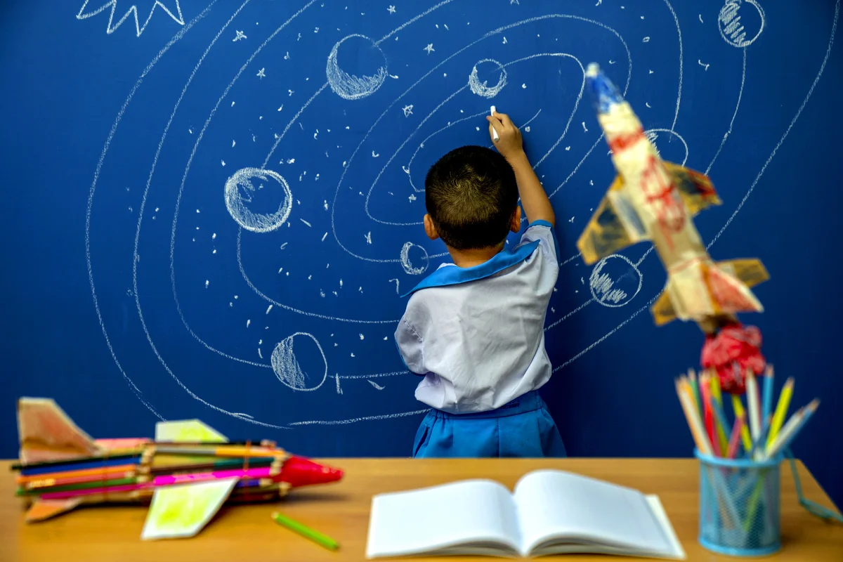 Little boy reaching for rocket in drawn space