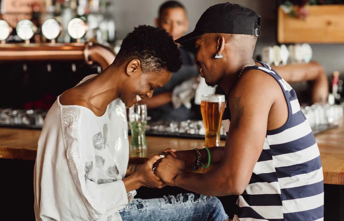 Beautiful smiling and affectionate couple holding hands whilst seated at bar drinking beer