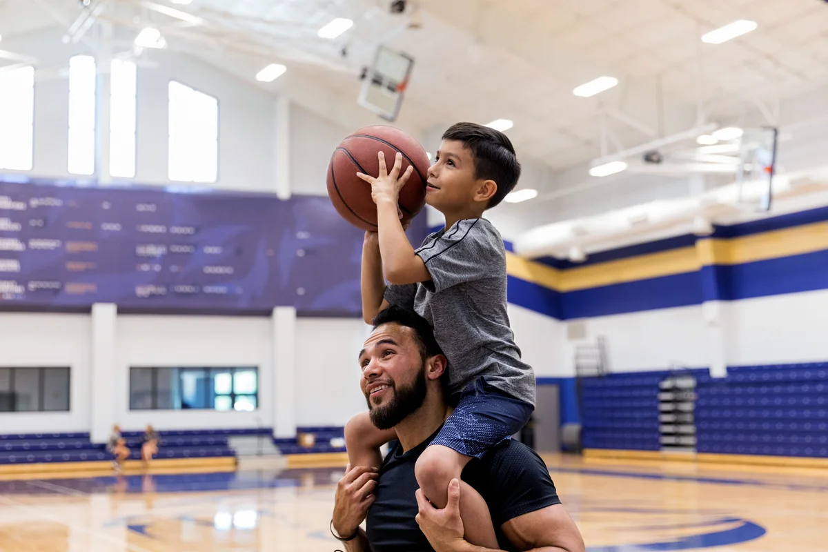Father has son on shoulders to shoot baskets at gym