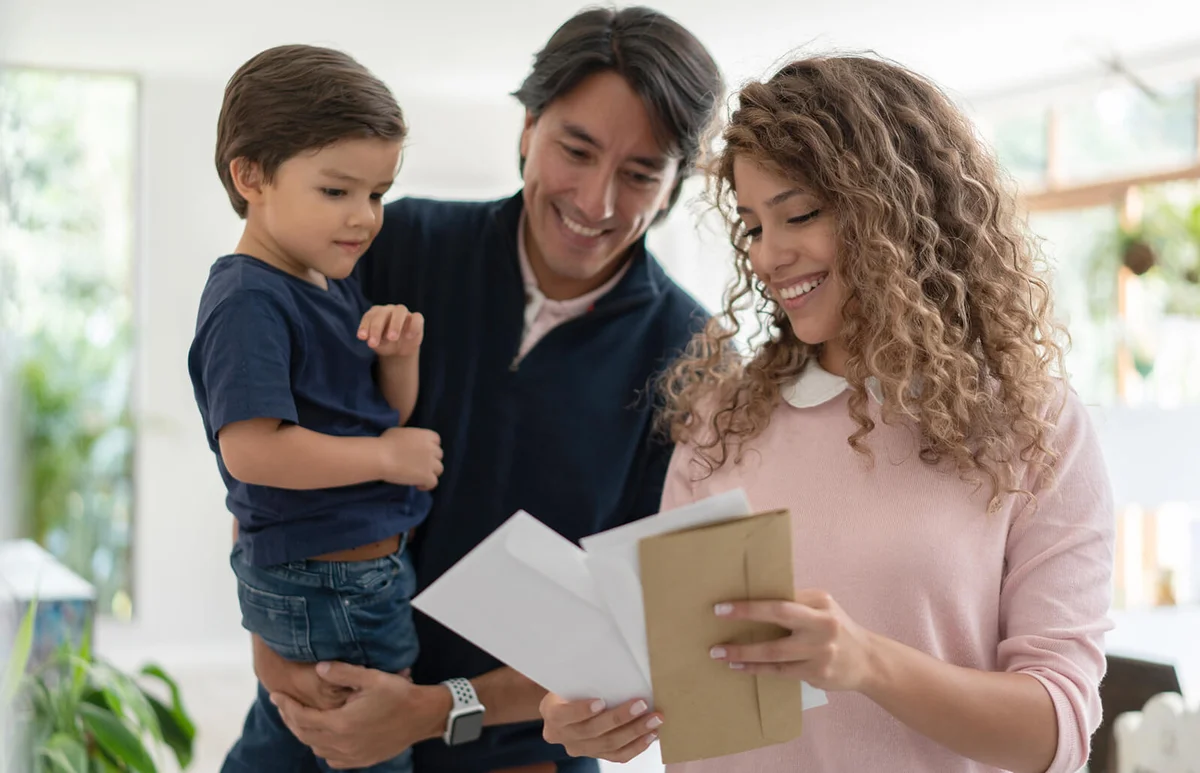 Beautiful woman showing partner the mail while he carries their son all smiling