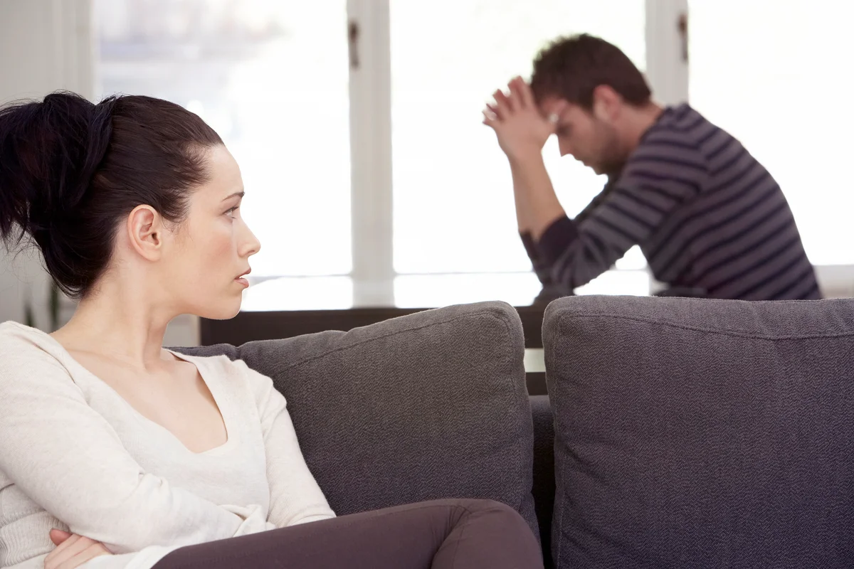Young woman sitting on sofa, looking at distressed man at table