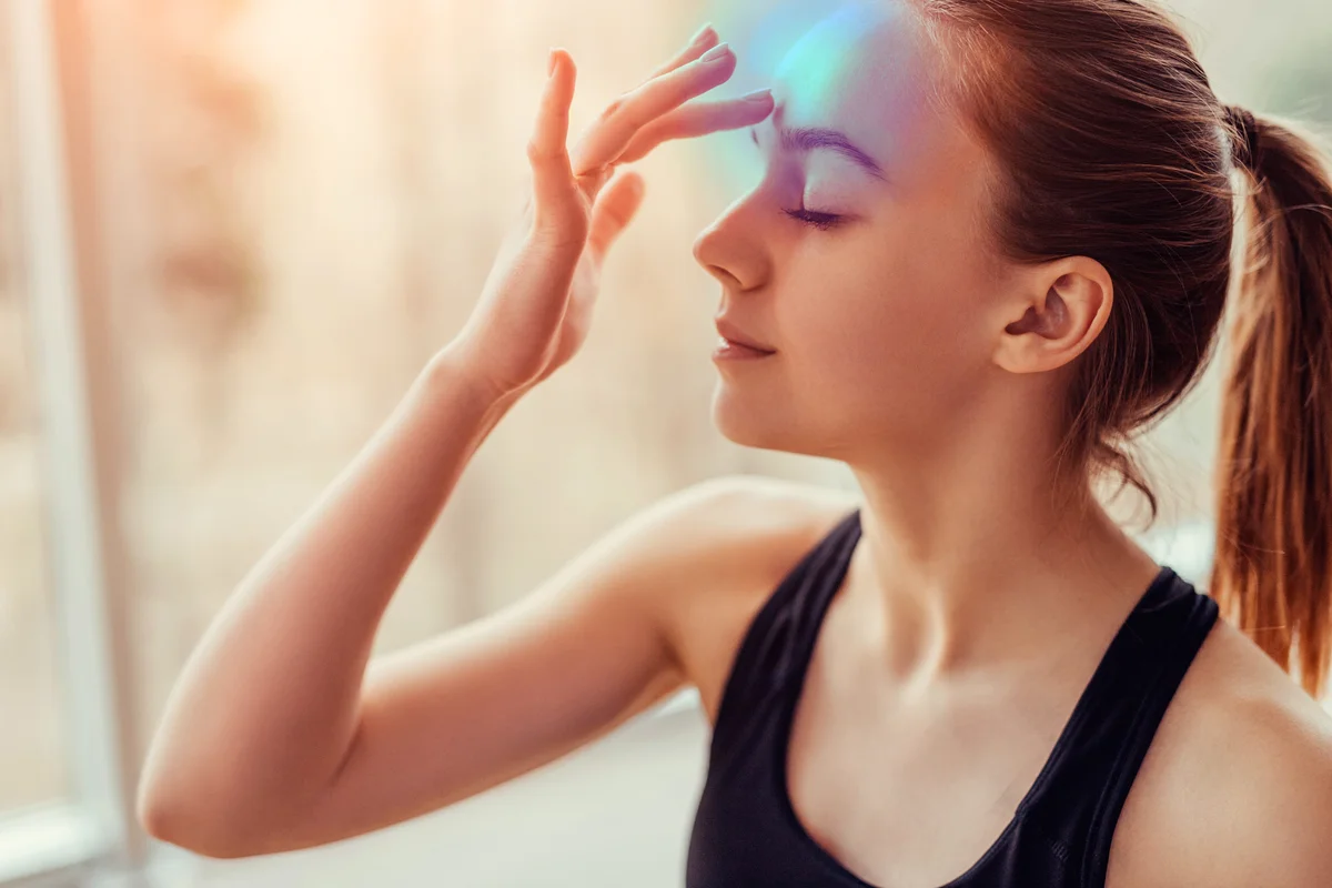 Young female with closed eyes touching chakra on forehead