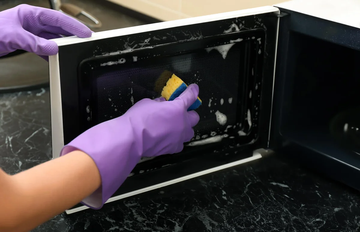 Young woman cleaning microwave oven in kitchen