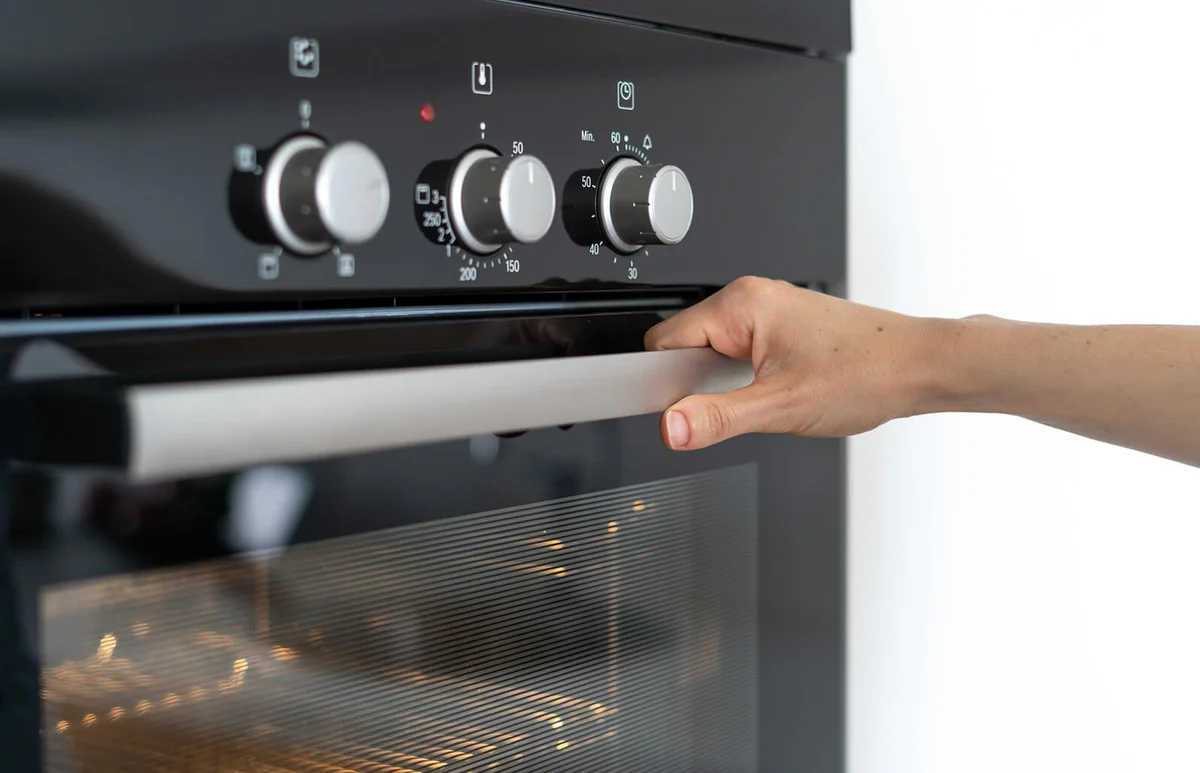 Woman holding handle modern built in oven and opening glass door