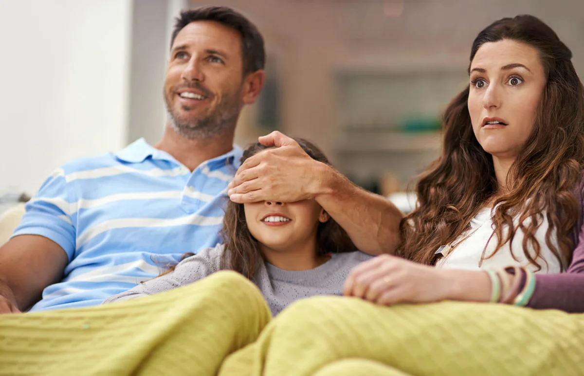 father covering his daughter's eyes while watching a movie