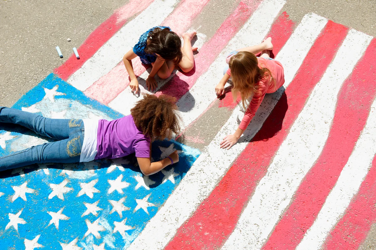 Girls with chalk coloring American flag on sidewalk
