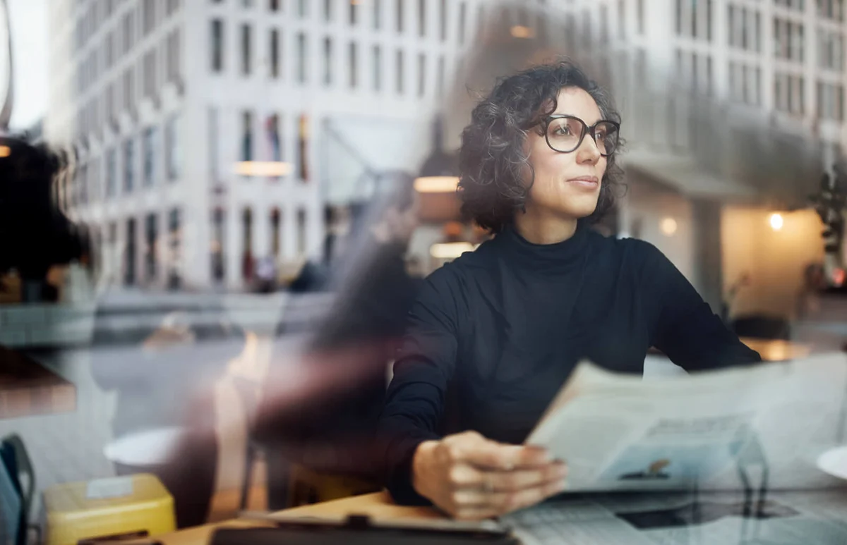 Mature businesswoman sitting inside at cafe with newspaper