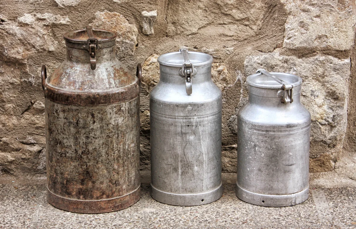 Three milk churns and stone wall as background