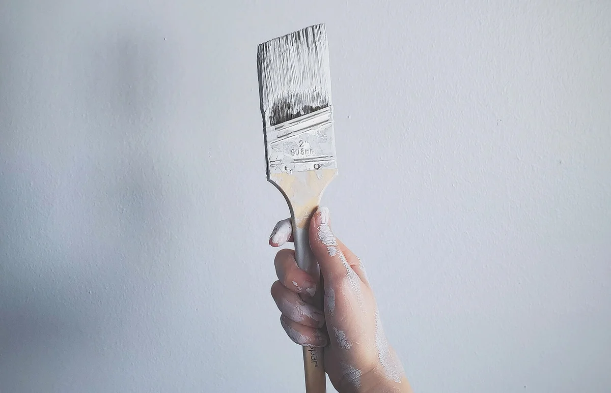 Woman Holding Paintbrush Against White Wall