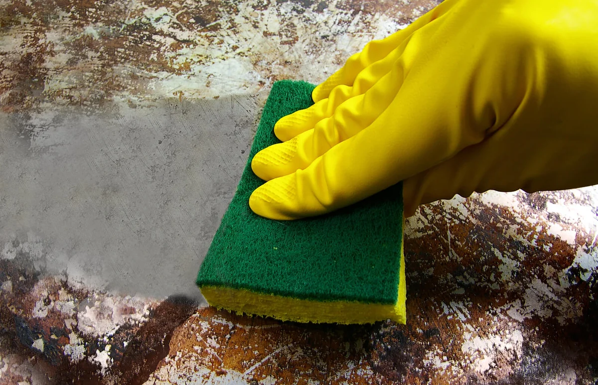gloved hand scrubbing a dirty metal surface