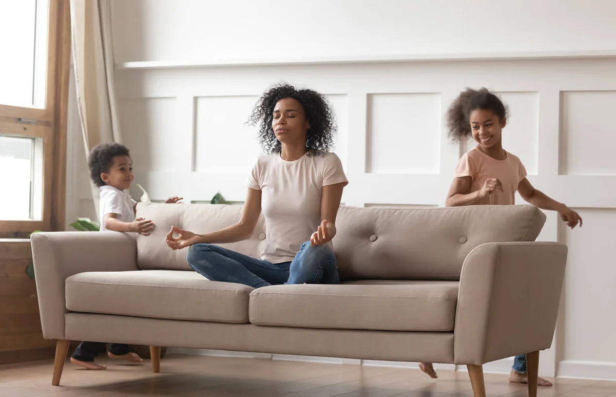 Calm mom doing yoga on sofa relaxing with kids