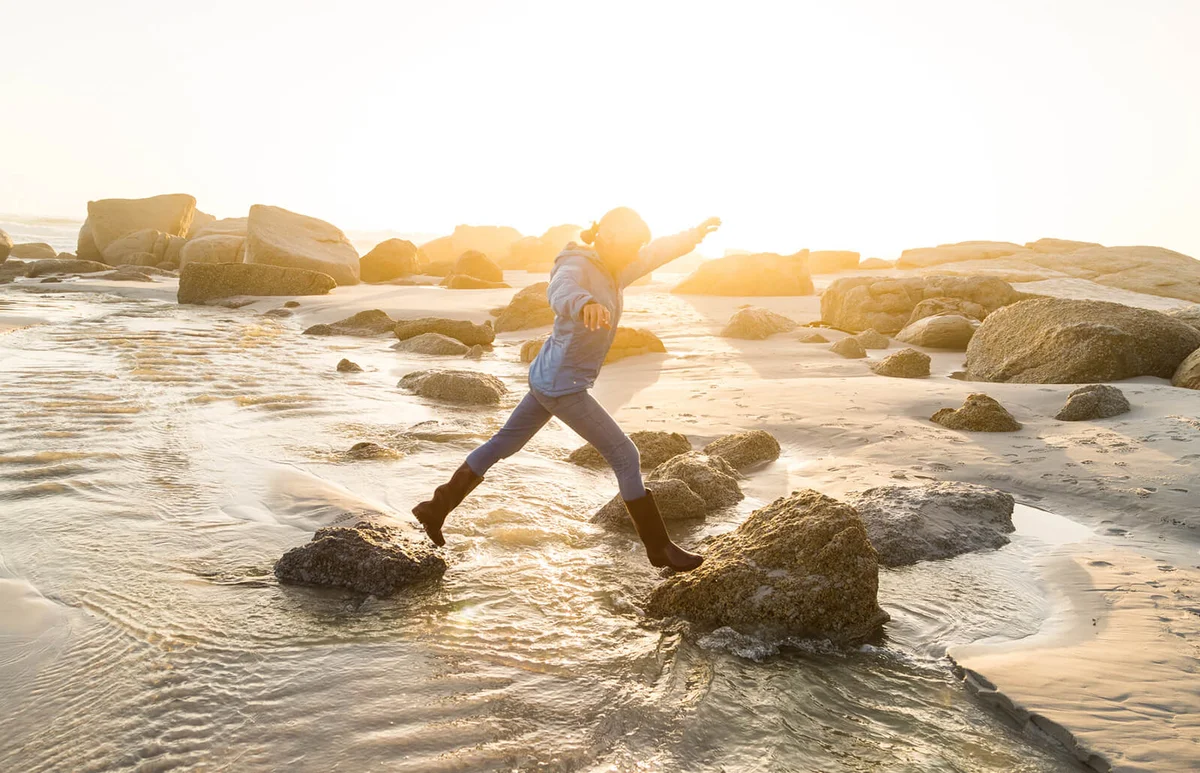 woman stepping across stream on the beach at sunset