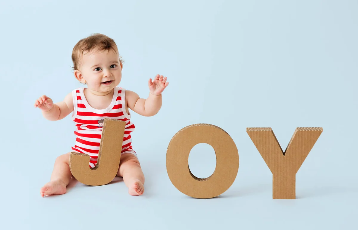 Baby boy playing with cardboard letters forming the word 'Joy'