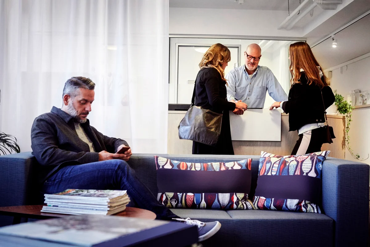 Mother and daughter talking to male therapist at reception while the father uses his phone