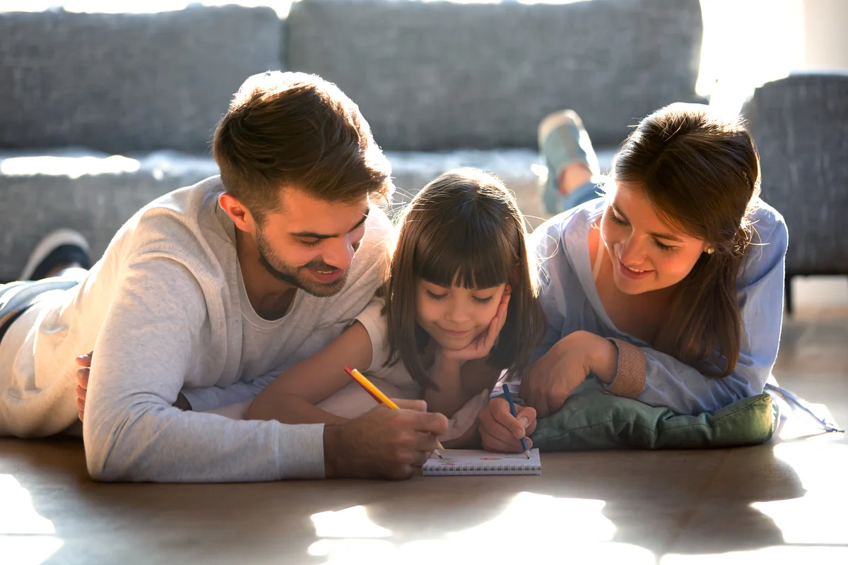 Couple and daughter lying on warm floor and drawing