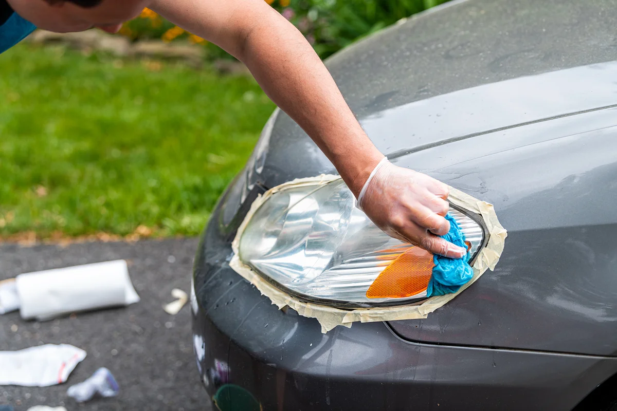 Man cleaning car headlights taped to protect paint rubbing with blue shop towel