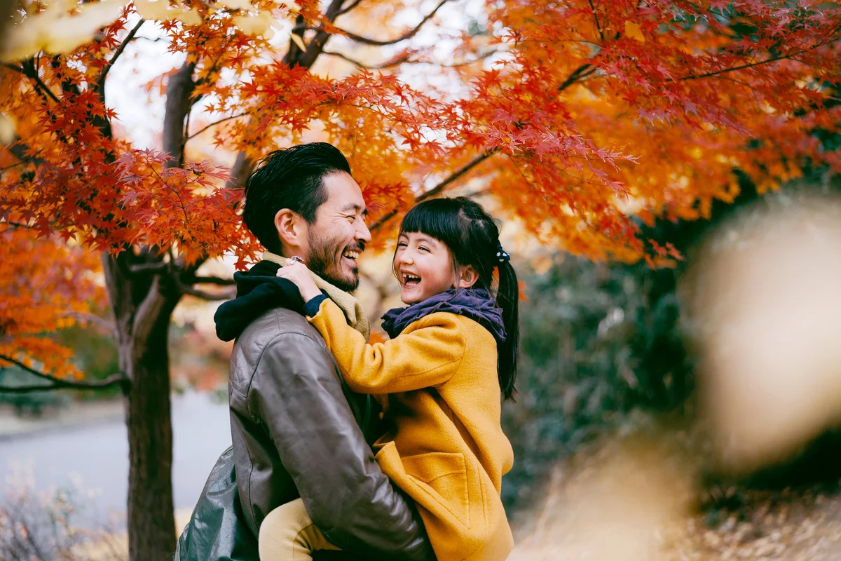 Father holding cheerful little girl under autumn leaves
