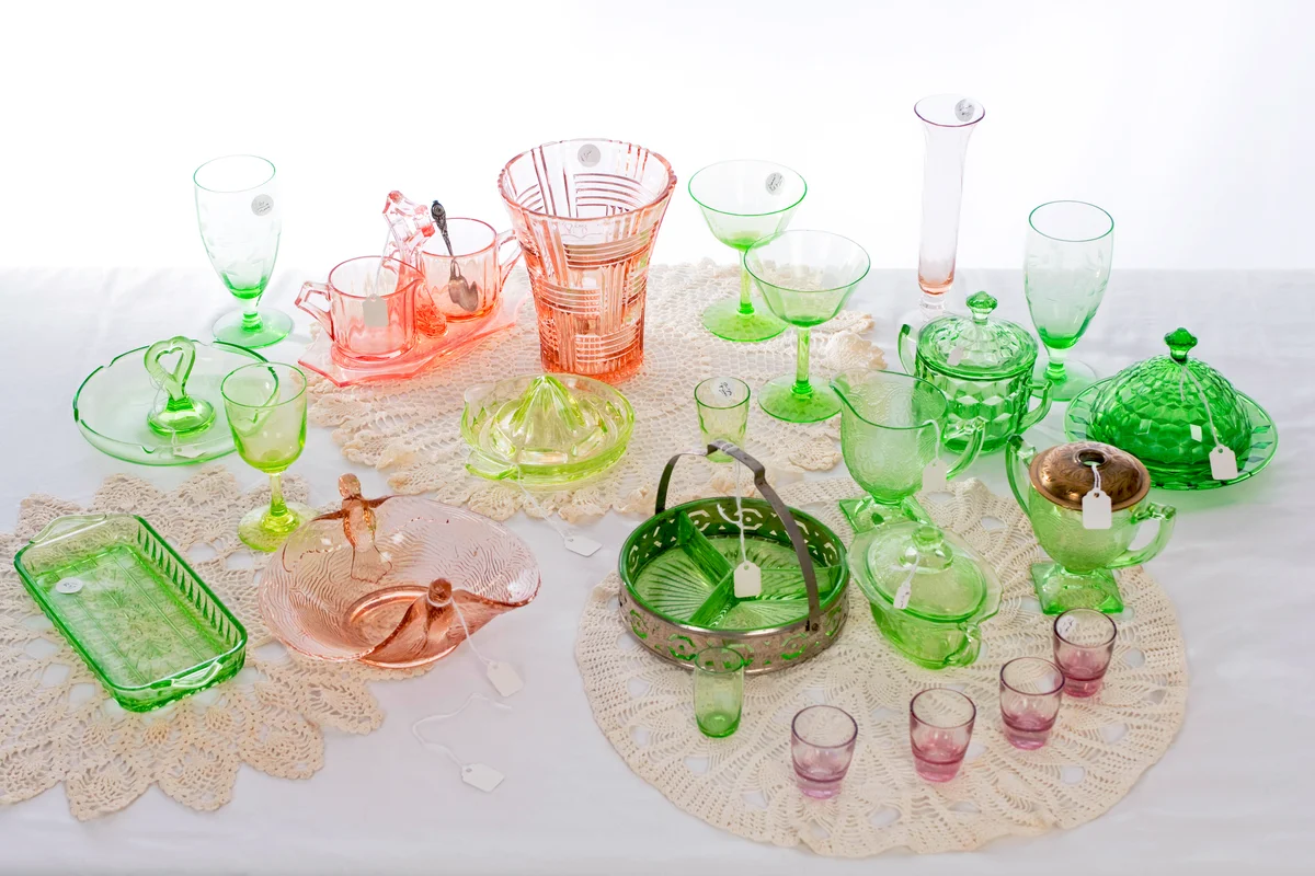 A table with a variety of pink and green American Depression glass at an estate sale